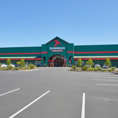 The storefront of the large Bunnings Warehouse in Hamilton South, showing the main entrance, signage, and extensive customer car park on a sunny day.